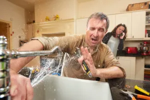 In a warm and inviting Lafayette, IN kitchen, a man grapples with a torrent of water gushing from a broken sink faucet. With determination in his eyes, he clutches a wrench, attempting to conquer the unexpected plumbing mishap. Amidst the chaos of scattered tools and household items, a woman stands in the background urgently making a phone call for assistance. The scene captures the essence of everyday life as teamwork and resilience come to the forefront amidst domestic challenges.