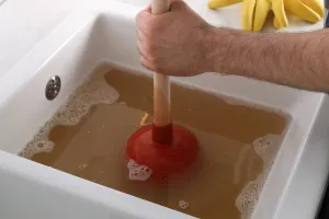 In this captivating image set in Lafayette, IN, a determined individual confronts a sink brimming with murky water, employing trusted plumbing techniques to restore order. The scene highlights the urgency and expertise involved in tackling such household issues. Nearby, a vibrant pair of yellow rubber gloves awaits eagerly on the countertop, symbolic of readiness and resilience in addressing any plumbing challenge that arises.